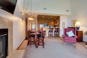 A living room with a fireplace, a dining area with wooden chairs, a kitchen with wooden cabinets, and a red armchair. - 1BR Lakeview 2nd-Floor - Balcony - Pool (Chelan)