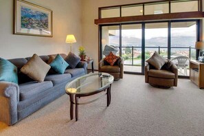 A living room with a sofa, two armchairs, a glass coffee table, and a view through large windows. - 1BR Lakeview 2nd-Floor - Balcony - Pool (Chelan)