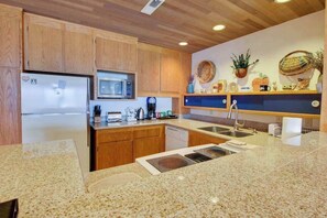A kitchen with wooden cabinets, a stainless steel refrigerator, a microwave, a sink, and a countertop with various items. - 1BR Lakeview 2nd-Floor - Balcony - Pool (Chelan)