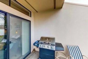 A balcony with a barbecue grill, a glass door, and a striped chair. - 1BR Lakefront - Pool - Hot Tub - Game Room (Chelan)