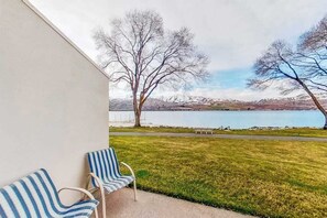 A balcony with two striped chairs overlooking a lake and mountains. - 1BR Lakefront - Pool - Hot Tub - Game Room (Chelan)