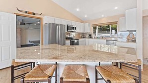 Uma cozinha moderna com armários brancos, eletrodomésticos de aço inoxidável e uma grande ilha com banquetas.