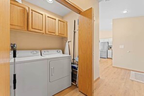 Un espace buanderie équipé d’un lave-linge et d’un sèche-linge, de placards en bois et d’une porte donnant sur la cuisine.