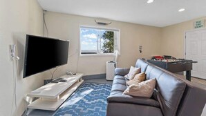 Uma sala de estar com televisão de tela plana, um sofá, uma mesa de pebolim e uma janela com vista.