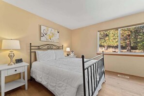 A bedroom with a bed, bedside table, lamp, and a window with a view of trees. - Large 2BR Lakeview - Hot Tub - Deck - Game Room (Chelan)