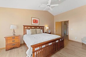 Une chambre à coucher avec un lit en bois, des tables de chevet, un ventilateur de plafond et une porte donnant sur une autre pièce.