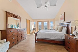 Quarto com cama grande, cómoda de madeira e ventoinha no teto.