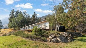 Uma casa moderna com varanda, rodeada por árvores e um gramado.