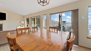Uma sala de jantar ampla com uma grande mesa de madeira e cadeiras, um lustre e janelas amplas que oferecem vista para o exterior.