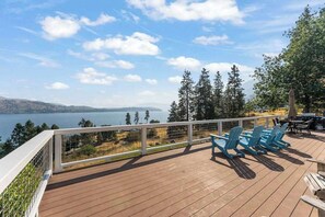 A wooden deck with blue chairs and a table, overlooking a lake with trees and hills in the background. - Large 2BR Lakeview - Hot Tub - Deck - Game Room (Chelan)