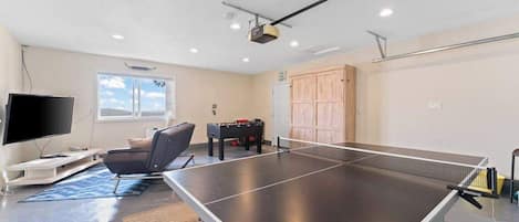 Una habitación con mesa de ping pong, televisor, sofá y mesa de futbolín.