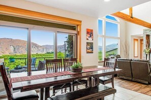 A dining area with a large table and chairs, a sofa, and a view of mountains through large windows. - 4BR Mountainview Dog Friendly - Chef's Kitchen (Orondo)