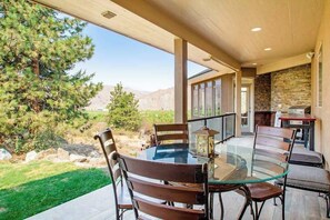 A glass-top dining table with chairs, a stone wall, and a view of a mountainous landscape.