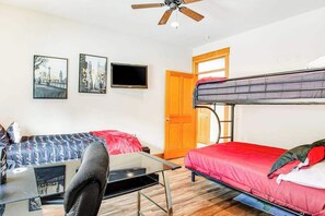Ein Zimmer mit einem Etagenbett, einem Schreibtisch mit Stuhl, einem Flachbildfernseher und zwei gerahmten Bildern an der Wand.