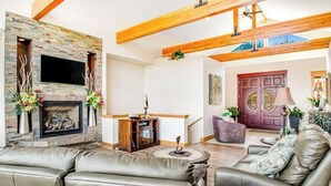Un salon doté d’une cheminée, de canapés en cuir, d’un plafond en bois et d’une porte avec une fenêtre.