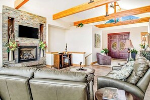 Ein Wohnzimmer mit Kamin, Ledersofas, Holzbalkendecke und einer Tür mit Fenster.
