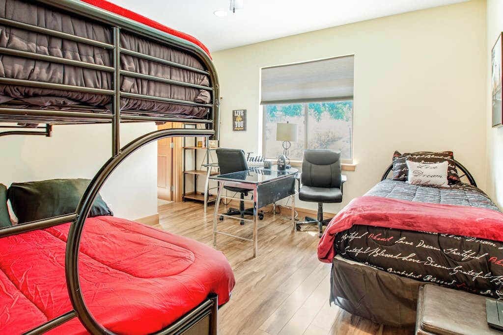 A room with bunk beds, a desk, a chair, and a window with blinds.
