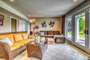 Ein geräumiges Wohnzimmer mit einer großen Couch, einer kleineren Couch und einem Couchtisch. Zwei Wanddekorationen und eine Lampe auf einem Beistelltisch sind ebenfalls vorhanden.
