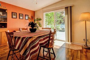A dining area with a striped tablecloth, wooden chairs, a potted plant, and a view through a glass door.
