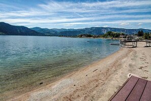 A lake with a pebbly shore, a wooden deck, and mountains in the background.