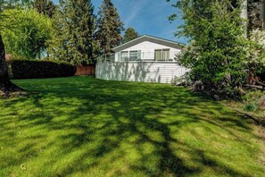 A residential property with a well-maintained lawn, a detached house with a gabled roof, and a wooden fence. - 3BR Lakefront - Dock - Deck - Firepit - W&D (Manson)
