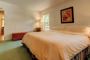 A bedroom with a large bed, a bedside table, a chair, and a window. - 3BR Lakefront - Dock - Deck - Firepit - W&D (Manson)