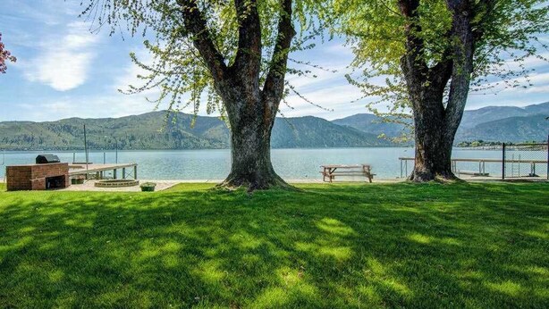 Un espacio al aire libre junto al lago con una terraza de madera, una parrilla y una mesa de picnic.