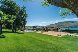 A park with a playground, a swimming pool, and a view of a lake and hills. - Luxe 1BR Lakeview - Patio - Pool - (Chelan)