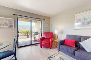 A room with a glass door leading to an outdoor area, a red chair, a dark-colored sofa with a red pillow, and a table with a lamp. - Luxe 1BR Lakeview - Patio - Pool - (Chelan)
