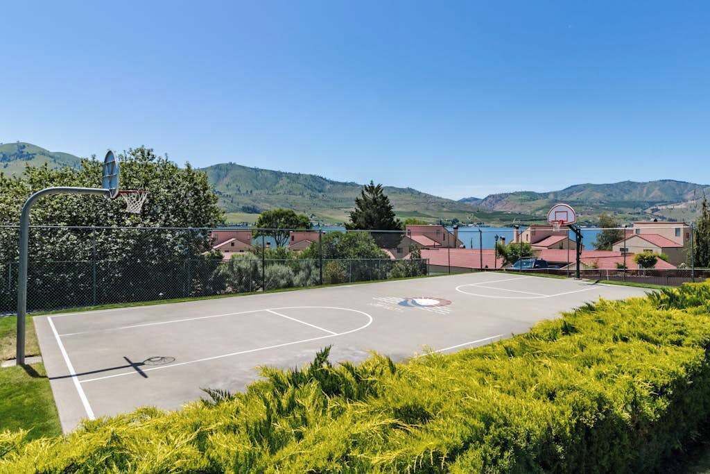 An outdoor basketball court with a clear view of the surrounding landscape, including hills and residential buildings.