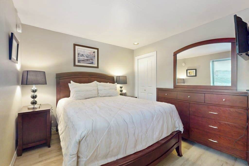 Un dormitorio con cama, lámparas de noche, cómoda, espejo y un cuadro en la pared.
