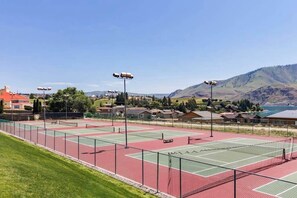 Een tennisbaan met een helder uitzicht op omliggende huizen en bergen.