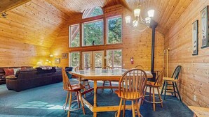 Ein Holzhütten-Interieur mit Esstisch, Stühlen, einer Couch und großen Fenstern.