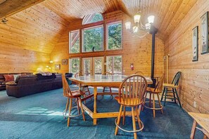 A wooden cabin interior with a dining table, chairs, a sofa, and large windows. - Spacious 3BR Mountainview - Fireplace - Deck (Leavenworth)