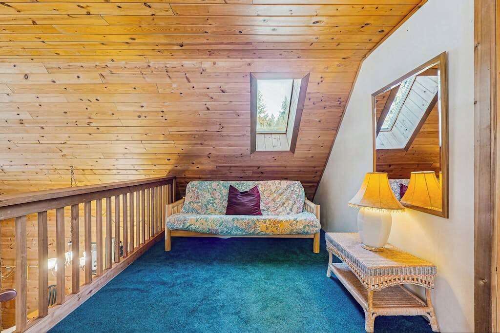 Une pièce avec un plafond en pente, un banc en bois, un canapé avec un coussin et une petite table avec une lampe.