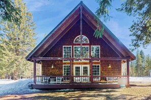 Une cabane avec un toit à pignon, une véranda avec des balustrades et une grande fenêtre en arc de cercle.