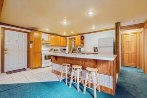 Une cuisine avec des meubles en bois, un îlot central doté de tabourets, un réfrigérateur et un four à micro-ondes.