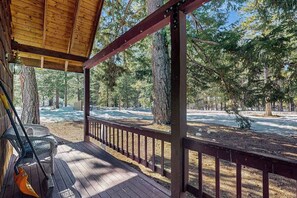 A covered outdoor area with a wooden deck, metal chairs, and a view of a forested area with a river. - Spacious 3BR Mountainview - Fireplace - Deck (Leavenworth)