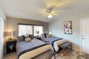 Une chambre avec deux lits, un ventilateur de plafond, une fenêtre et une porte.