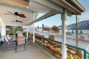 Een balkon met zitplaatsen, een plafondventilator en uitzicht op een weg en een waterpartij.