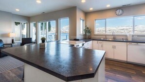 Uma cozinha moderna com uma ilha grande, armários brancos e vista para uma paisagem nevada através de amplas janelas.