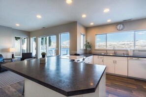 A modern kitchen with a large island, white cabinetry, and a view of a snowy landscape through large windows. - Lakefront 3BR with private dock & amazing views (Chelan)