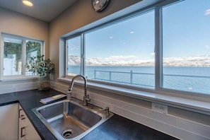 A kitchen with a large window, a stainless steel sink, and a view of a lake with mountains. - Lakefront 3BR with private dock & amazing views (Chelan)