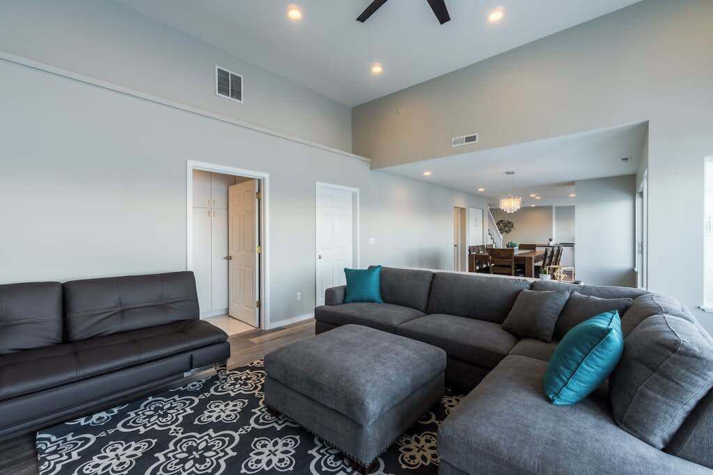 A modern living room with a grey sectional sofa, a black sofa, and a patterned rug.