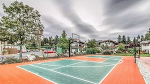 En utomhusbasketplan med en grön och orange yta, omgiven av träd och bostadshus.
