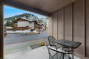 A view from a balcony with a table and chairs, overlooking a building with a snow-covered roof and a parking area. - Downtown Studio Mountainview 1st-Floor - Patio (Leavenworth)