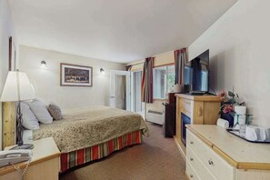 A bedroom with a bed, bedside table, lamp, TV, dresser, and a framed picture on the wall. - Downtown Studio Mountainview 1st-Floor - Patio (Leavenworth)