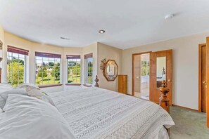 A bedroom with a large bed, a wooden dresser, a mirror, and a door leading to an outdoor area. - Spanish-style 6BR Mountainview - Deck - W&D (East Wenatchee)