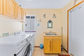 A compact kitchen with a washing machine, wooden cabinets, a sink, and decorative wall art.