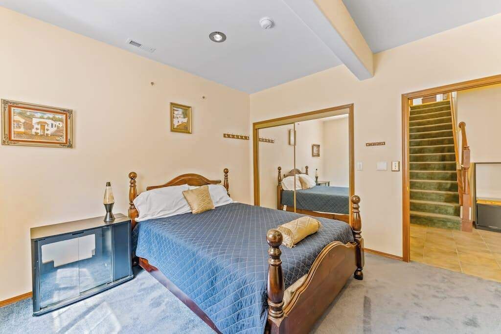 Een slaapkamer met een bed, nachtkastje, spiegel en een trap.